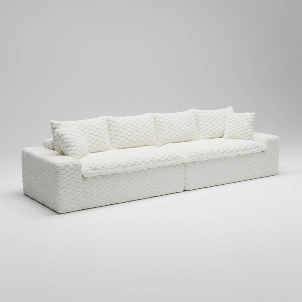 A cream-colored textured sectional sofa slipcover with matching throw pillows, shown fitted on a modular sofa in a bright, modern living room setting.